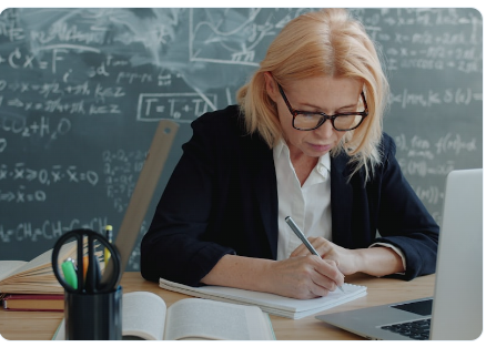 Maestra escribiendo en un cuaderno con pizarra al fondo